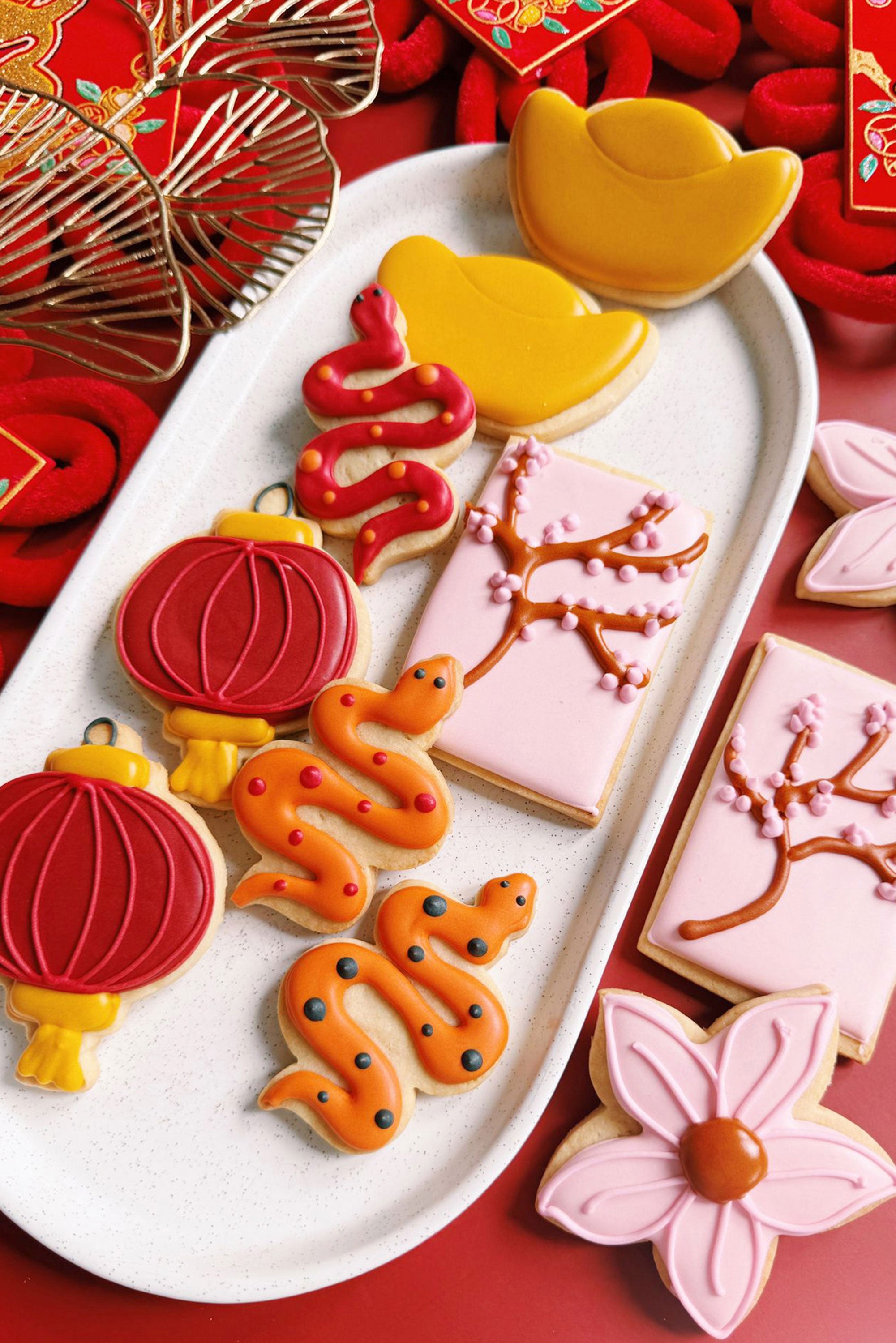 Decorative cookies shaped like traditional Chinese elements on a white plate with a red background.