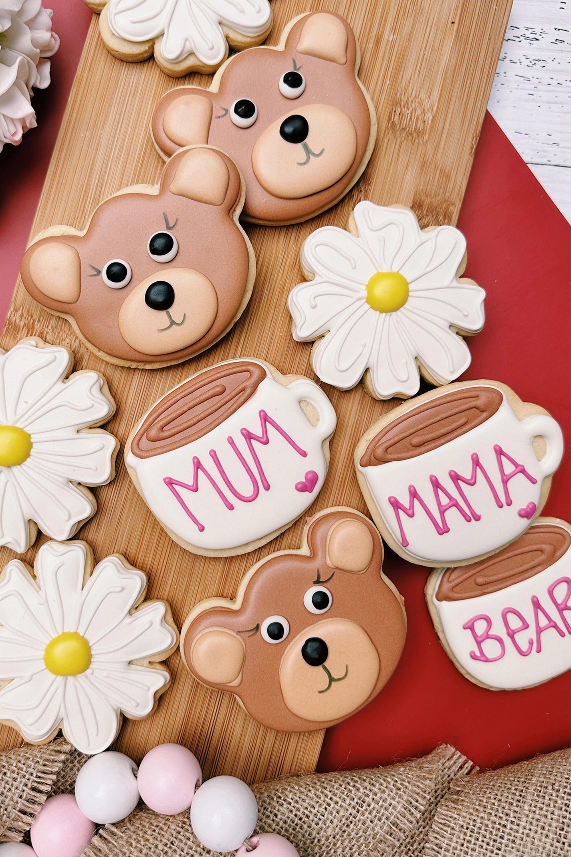 Decorative cookies shaped like bears and mugs with 'MUM', 'MAMA', and 'BEAR' text on a wooden board.