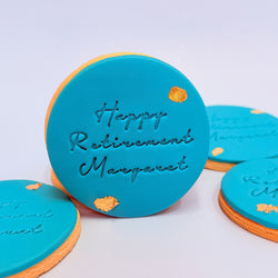 Blue cookies with 'Happy Retirement Margaret' text on a light purple background